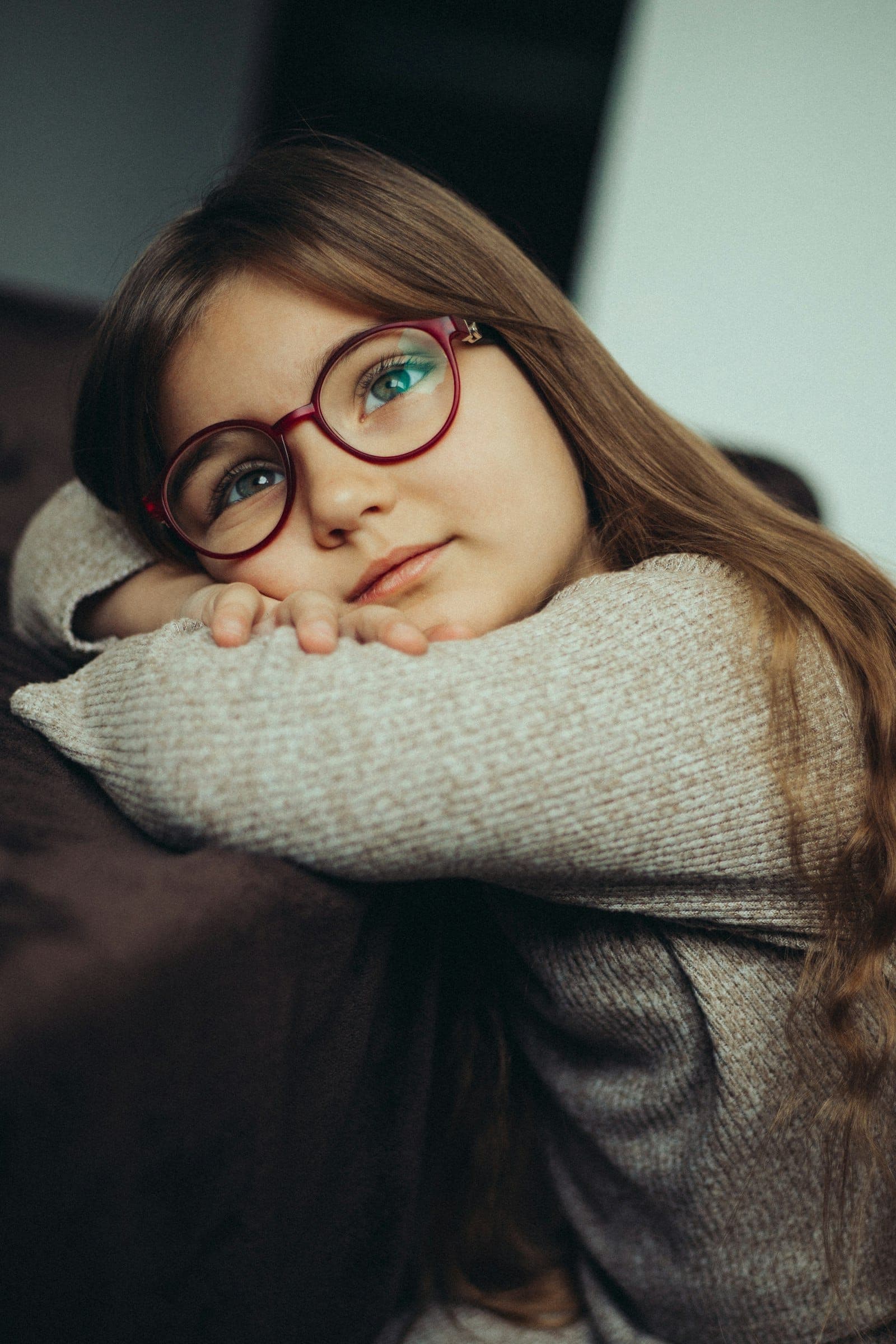 Girl in red round eyeglasses resting her chin on her arms