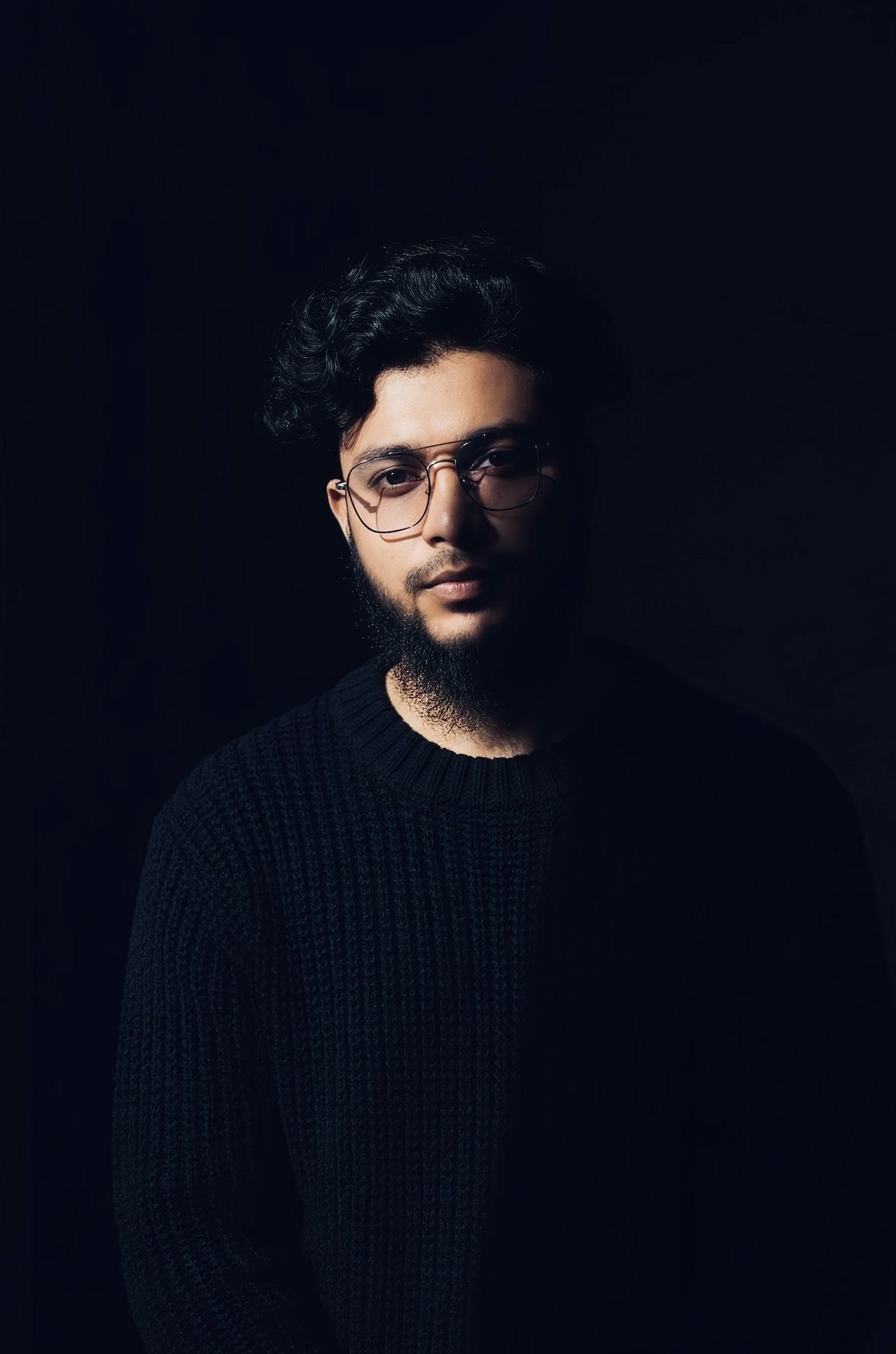 Man with curly hair wearing thin metal eyeglasses in low light